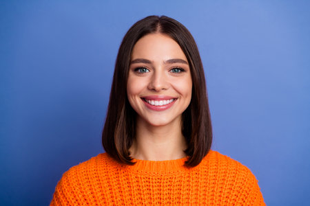 Portrait of a Young Woman in an Orange Sweater Smiling Against a Purple Background, Styled with Bob Hair and Autumn Fashionの写真素材
