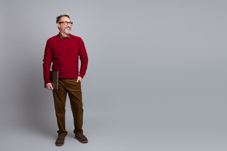 Middle-aged professional man with glasses holding a laptop posing confidently against a gray studio backdropの写真素材