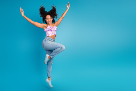 Young stylish woman jumps against blue background wearing a purple top and light jeans for vibrant...
