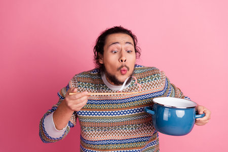 Young Stylish Man in Vibrant Sweater Enjoying Soup on Pink Background, Expressing Fun and Casual Lifestyleの写真素材