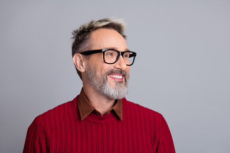 Mature professional man wearing glasses with confident smile in red sweater against plain gray studio backgroundの写真素材