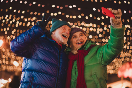 Funny heartwarming winter selfie with grandparents under twinkling Christmas lights at a festive...