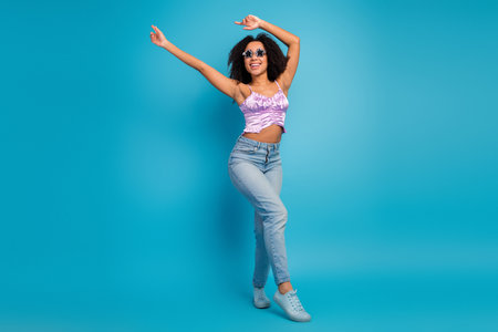 Young woman dancing in jeans against a blue background showcasing carefree summer style and fashion glamourの写真素材