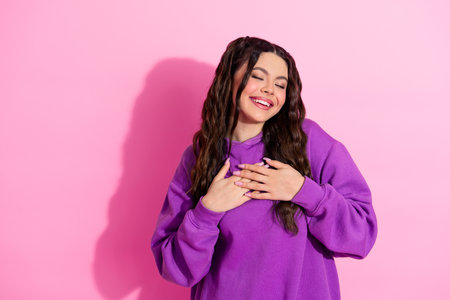 Young brunette woman in a stylish purple sweatshirt smiling joyfully with a pink background expressing happiness and charmの写真素材