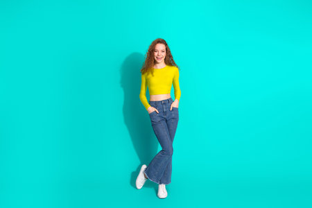 Young woman posing confidently against a vibrant turquoise background wearing a yellow top and...