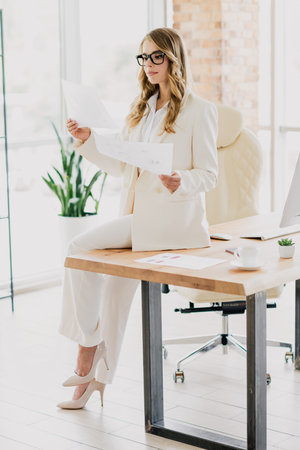 Confident businesswoman in elegant formalwear analyzing documents while seated in a modern and tidy office settingの写真素材