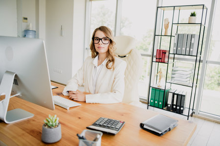 Elegant confident businesswoman working in a modern office environment, seated at a desk with professional demeanorの写真素材