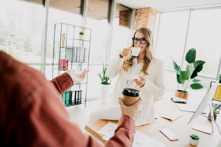 Confident businesswoman in stylish formalwear enjoying coffee during a professional discussion in a modern office interiorの写真素材