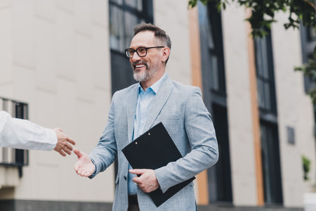 Businessman shakes hands in a modern city street scene outside a stylish office building showing...