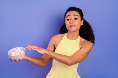 Young woman posing with a bowl of marshmallows in a bright yellow dress against a purple backgroundの写真素材