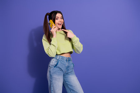 Cheerful young woman in casual style talking on smartphone against a vibrant purple background