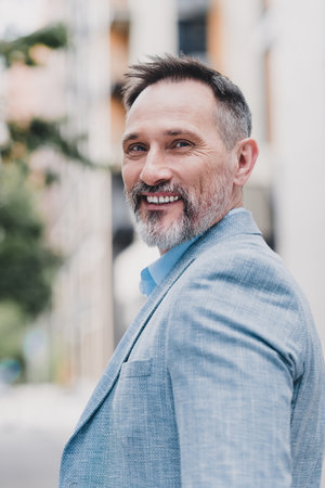 Confident mature businessman in stylish blue suit poses in city street showcasing professional...