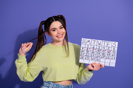 Smiling young woman wearing casual fashion holding calendar against vibrant purple background