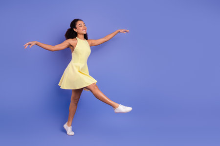 A cheerful young woman in a yellow dress dancing joyfully on a violet background demonstrating happiness and styleの写真素材
