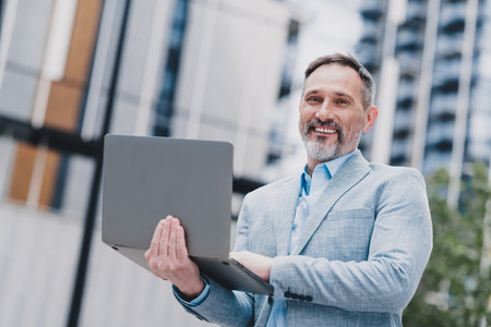 Confident modern businessman outdoors in city urban setting presenting laptop for executive work and real estate career in megapolis environmentの写真素材