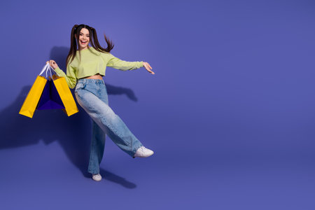 Energetic young woman holding colorful shopping bags with a bright smile on a vibrant purple backdropの写真素材