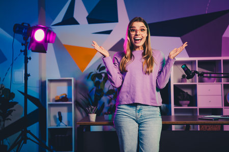 Confident young woman in a creative studio with microphone streaming live content featuring vibrant neon lightingの写真素材