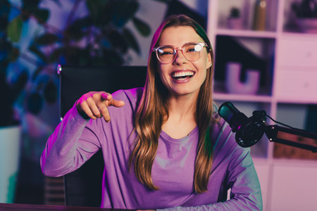 Popular blogger with glasses smiling confidently while streaming with a microphoneの写真素材