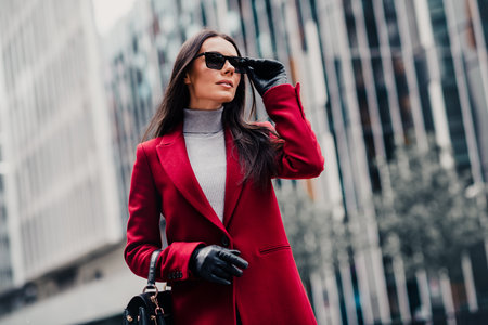 Elegant woman in a red coat walking in a modern urban setting exuding high fashion style and sophistication outdoorsの写真素材