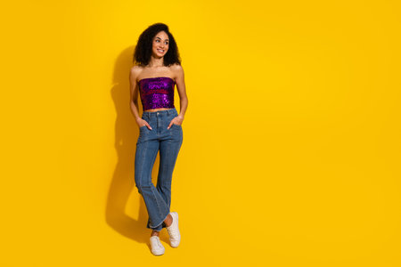 Bright confident young woman wearing a purple sequin top and blue jeans against a bold yellow background for a vibrant fashion and lifestyle imageの写真素材