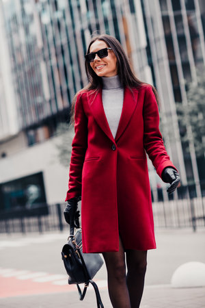 Confident woman wearing red coat and sunglass walking stylishly in urban setting with high fashion chicの写真素材