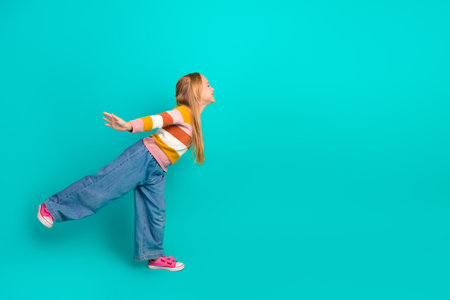 Cheerful young girl posing energetically against a vibrant teal background in stylish casual wear, expressing fun and spontaneityの写真素材