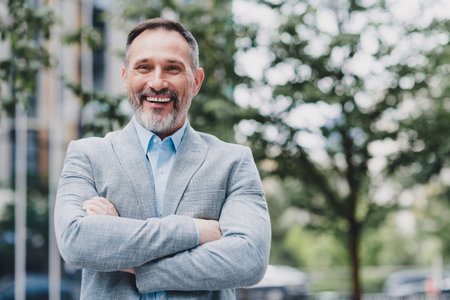 Confident modern businessman stands in a stylish suit with arms crossed in an urban city setting smiling at the cameraの写真素材
