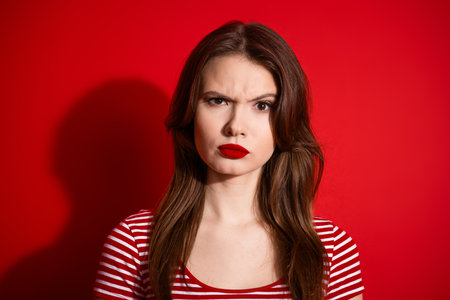 Portrait of a young brunette woman in red and white striped casual attire on a bold monochromatic red backgroundの写真素材