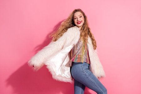 Young woman in a fashionable fur coat posing cheerfully against a vibrant pink background to showcase an elegant lifestyleの写真素材