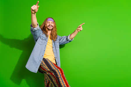 Cheerful man with a retro hippie style pointing with joyous expression against a vibrant green backgroundの写真素材