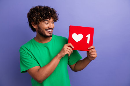 Cheerful young man in a green t-shirt holds a red heart icon sign expressing love and positivity...