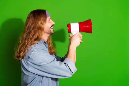 Attractive young man holding a loudspeaker promoting with enthusiasm against a green background, perfect for adsの写真素材