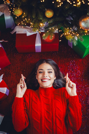 Playful festive moment as a woman in a red sweater smiles under a Christmas tree with gifts and...