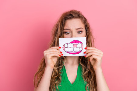Young woman with playful expression holding sketch of teeth against colorful background, showcasing fun and creativityの写真素材