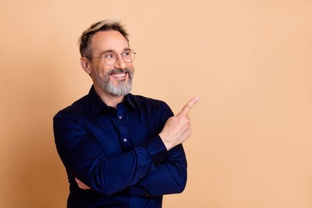 Middle-aged professional man in a formal shirt gesturing confidently against a beige background showcasing elegance and styleの写真素材