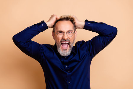 Excited businessman reacts with enthusiasm while holding his head and showing energy on a beige...