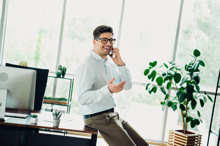 Young businessman conversing confidently on the phone in a stylish office with greenery and natural lightの写真素材