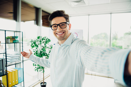 Confident young businessman in modern office smiling and gesturing enthusiastically while showcasing a successful professional atmosphereの写真素材