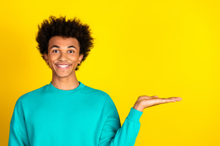 Young man gesturing with hand on bright yellow background while smiling, conveying cheerfulness and positivity in casual styleの写真素材
