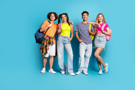 Four friends pose in a bright carefree group portrait showing youth style friendship and summer energy against a vivid blue backgroundの写真素材