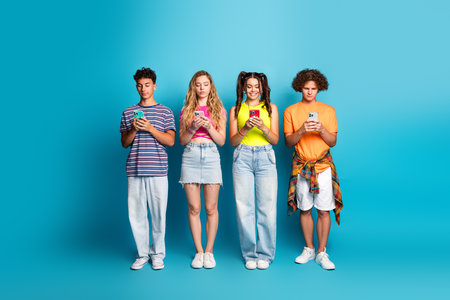 fun and friendly teens on a bright blue backdrop absorbed in their phones creating a playful modern youth momentの写真素材