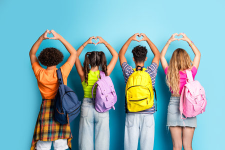 Playful group of friends making heart shapes with their hands against a bright blue wall showing...
