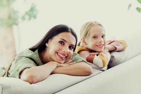 Mother and daughter enjoying quality time at home smiling together on couch in a bright living room spaceの写真素材