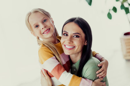 Loving mother and daughter smiling and hugging each other at home, enjoying a joyful day together, bonding warmly.の写真素材