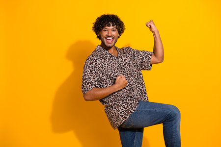 Energetic young man celebrates with arm gestures on vibrant yellow background showcasing style and personalityの写真素材