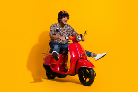 Cheerful young man on a red scooter over a vibrant yellow background, exuding confidence and style in a leopard print shirt.の写真素材