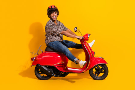 Happy young man on a vibrant red scooter posing against a bold orange background, embodying style and cheerful energyの写真素材