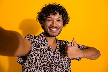 Smiling young man giving a thumbs-up gesture against a bright yellow backgroundの写真素材