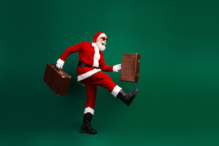 Santa Claus joyfully walking with suitcases against green background, showcasing holiday cheer and whimsical humor for the Christmas seasonの写真素材