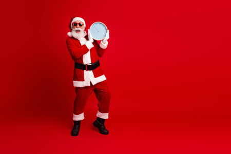 Santa Claus holds a clock wearing sunglass on a red background and promotes holiday cheer in a lively atmosphereの写真素材